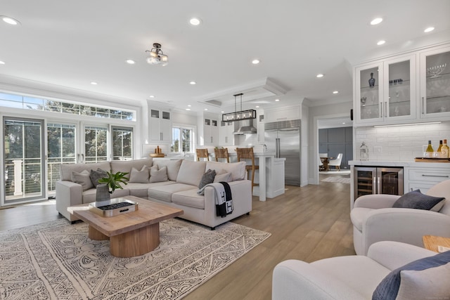 living room with crown molding, bar area, light hardwood / wood-style flooring, a tray ceiling, and beverage cooler