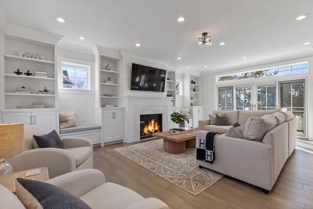 living room with built in features, crown molding, a high end fireplace, and light hardwood / wood-style floors