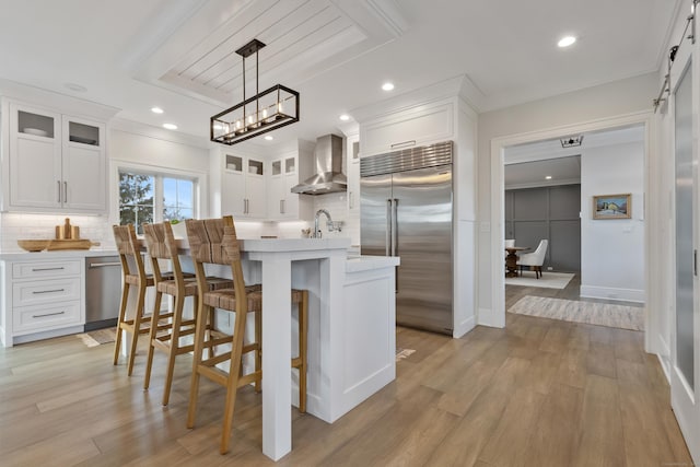 kitchen featuring white cabinetry, appliances with stainless steel finishes, a kitchen island, pendant lighting, and wall chimney range hood