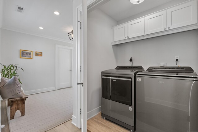 clothes washing area featuring cabinets, ornamental molding, light wood-type flooring, and washing machine and clothes dryer