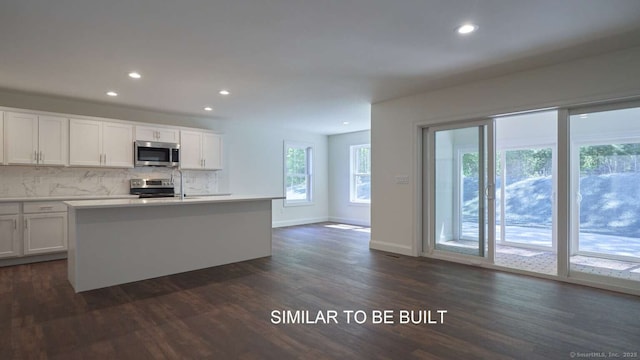 kitchen with backsplash, stainless steel appliances, an island with sink, and white cabinets