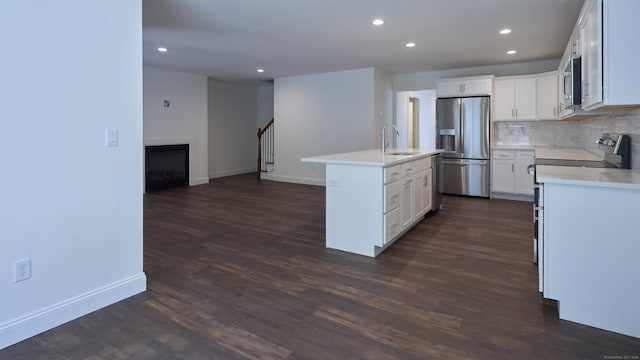 kitchen featuring appliances with stainless steel finishes, a sink, a kitchen island with sink, light countertops, and backsplash