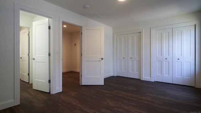 unfurnished bedroom featuring two closets, baseboards, and dark wood-style flooring