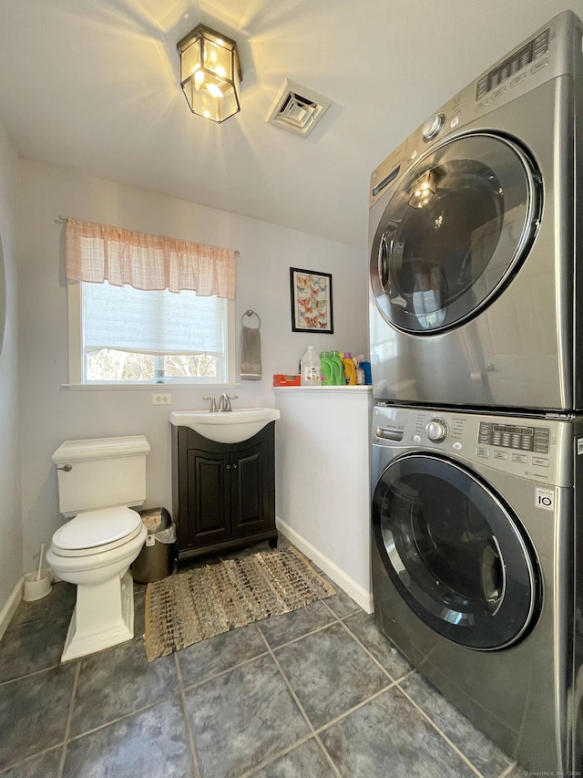 washroom featuring stacked washer / drying machine, dark tile patterned flooring, and sink