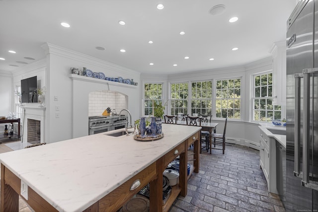 kitchen featuring crown molding, sink, an island with sink, and light stone counters