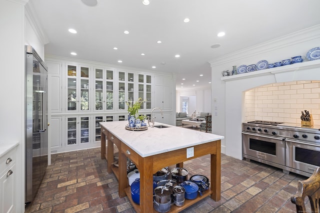 kitchen featuring white cabinetry, an island with sink, sink, premium appliances, and ornamental molding