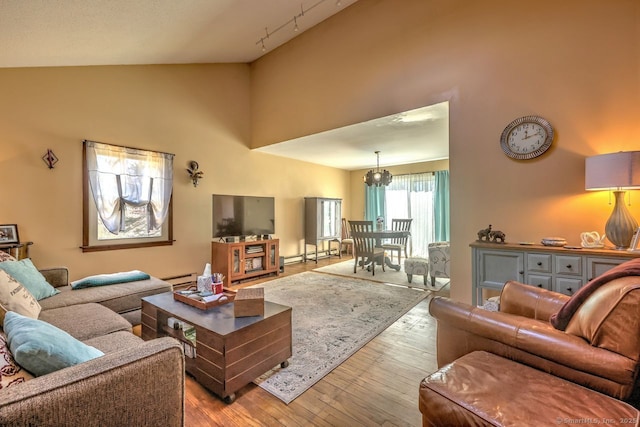 living room with a baseboard heating unit, light hardwood / wood-style flooring, high vaulted ceiling, and track lighting