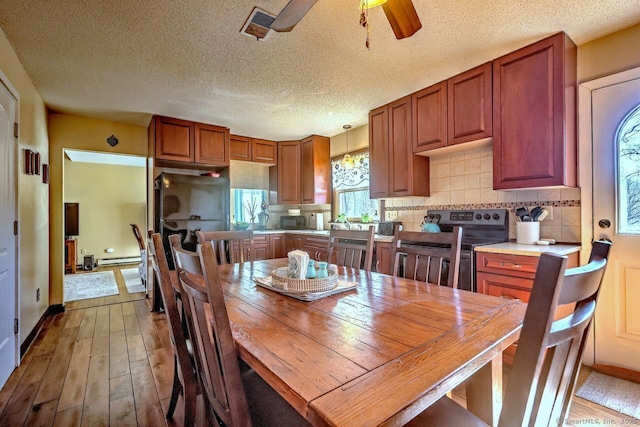 dining space with ceiling fan, wood-type flooring, a baseboard radiator, and a textured ceiling