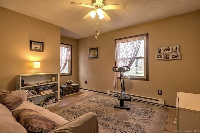 workout area with baseboard heating, ceiling fan, a textured ceiling, and light wood-type flooring