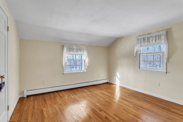 spare room featuring baseboard heating, vaulted ceiling, light hardwood / wood-style flooring, and a textured ceiling