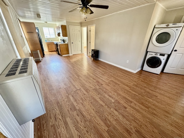 unfurnished living room featuring hardwood / wood-style flooring, crown molding, stacked washer and clothes dryer, and ceiling fan