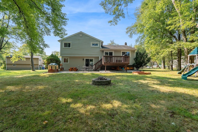 rear view of property with a playground, a deck, a fire pit, a yard, and a patio area