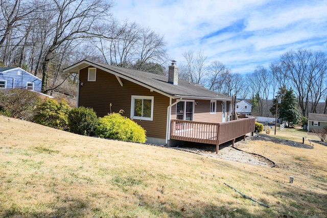 rear view of house featuring a chimney, a wooden deck, a yard, and a shingled roof