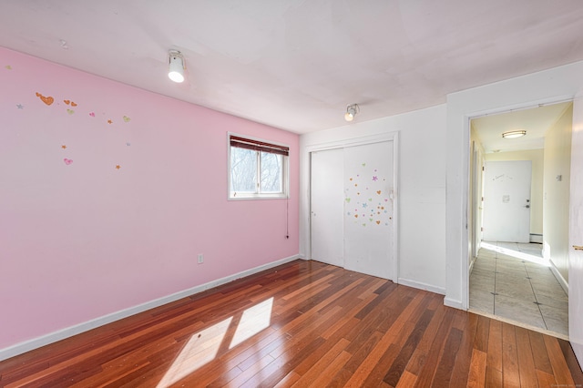 unfurnished bedroom featuring a closet, a baseboard heating unit, baseboards, and hardwood / wood-style flooring