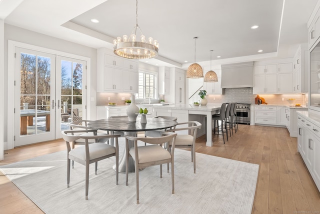 dining area featuring french doors, a tray ceiling, light hardwood / wood-style flooring, and a notable chandelier