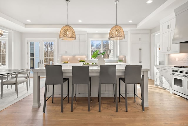 kitchen featuring premium range hood, tasteful backsplash, white cabinetry, high end stainless steel range oven, and hanging light fixtures