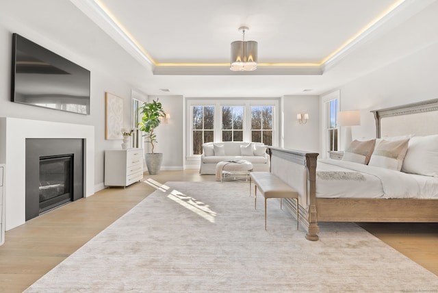 bedroom featuring a tray ceiling, light hardwood / wood-style floors, and multiple windows