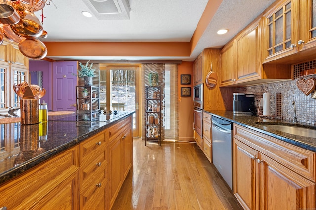 kitchen featuring sink, tasteful backsplash, light wood-type flooring, appliances with stainless steel finishes, and dark stone counters