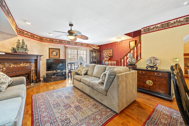 living room featuring ceiling fan, a high end fireplace, a textured ceiling, and light hardwood / wood-style flooring