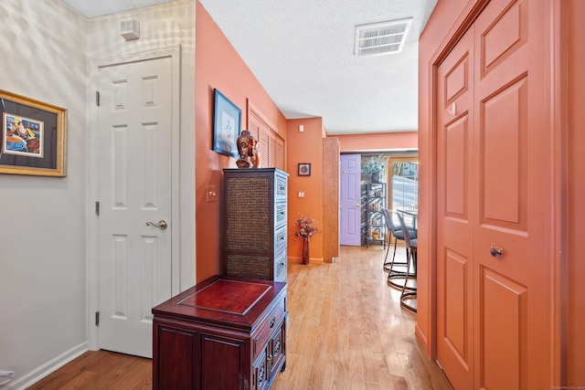 hall with a textured ceiling and light wood-type flooring