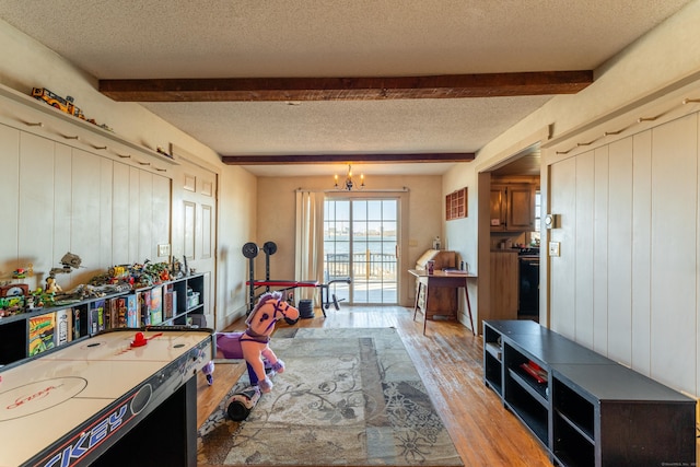 recreation room featuring beamed ceiling, light hardwood / wood-style floors, a textured ceiling, and a notable chandelier