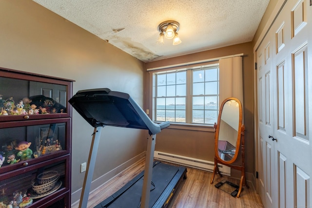 exercise room with a water view, hardwood / wood-style flooring, a textured ceiling, and a baseboard heating unit