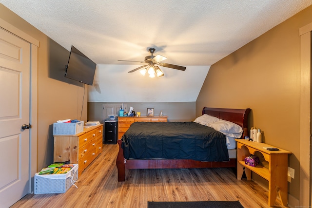 bedroom with vaulted ceiling, ceiling fan, a textured ceiling, and light hardwood / wood-style flooring