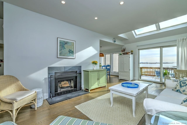 living room with lofted ceiling with skylight, a tile fireplace, and light wood-type flooring