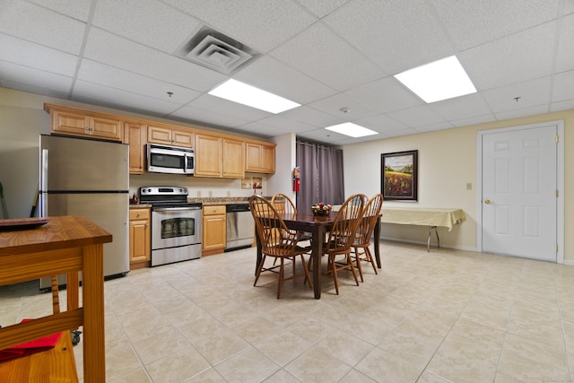 kitchen with light tile patterned floors, a paneled ceiling, and appliances with stainless steel finishes