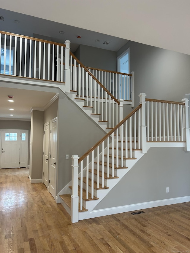 staircase featuring crown molding, hardwood / wood-style floors, and a high ceiling