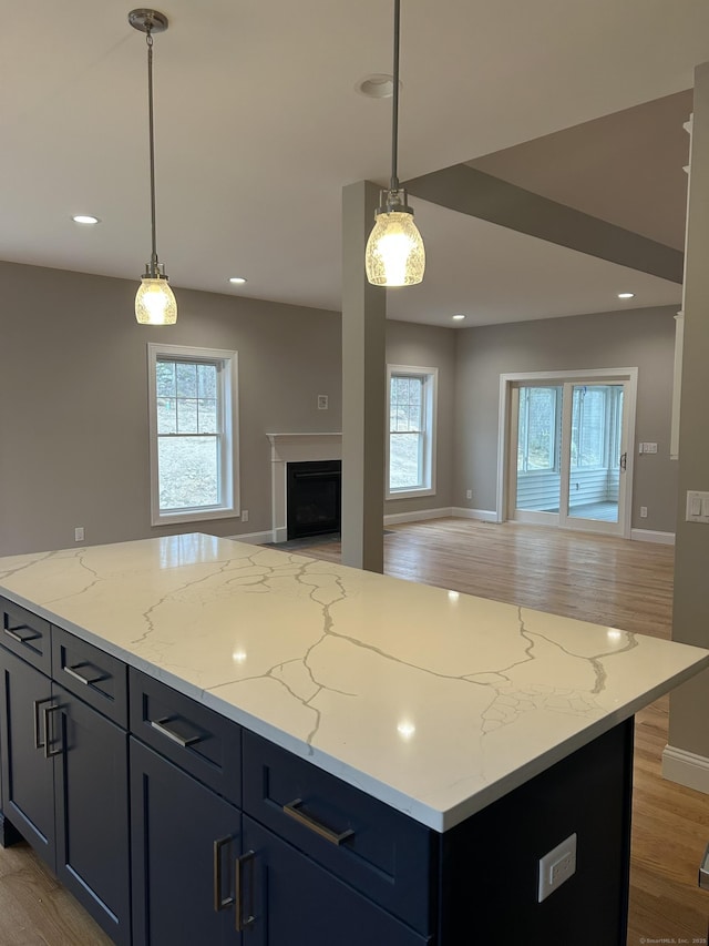 kitchen featuring decorative light fixtures, light stone countertops, a center island, and light wood-type flooring