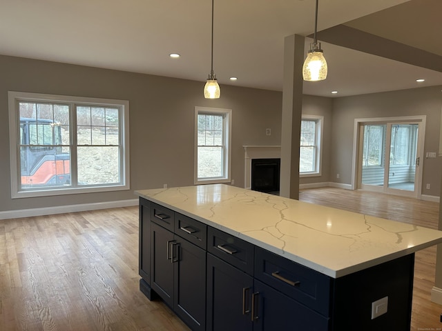 kitchen with light hardwood / wood-style floors, a kitchen island, light stone counters, and decorative light fixtures