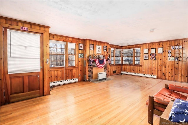 interior space with a baseboard heating unit, light wood-type flooring, and wood walls