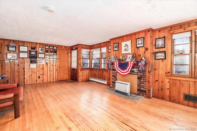 misc room featuring a baseboard radiator, light hardwood / wood-style floors, plenty of natural light, and a wood stove