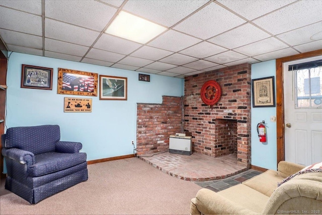 carpeted living room featuring a drop ceiling and a wood stove