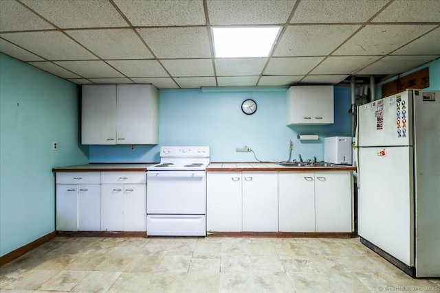 kitchen featuring white appliances, sink, a drop ceiling, and white cabinets