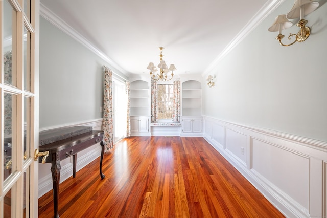 unfurnished living room with ornamental molding, hardwood / wood-style floors, built in features, and a chandelier