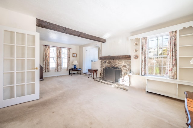 unfurnished room with a stone fireplace, carpet floors, and beamed ceiling