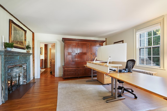 home office with radiator, wood finished floors, a warm lit fireplace, and baseboards