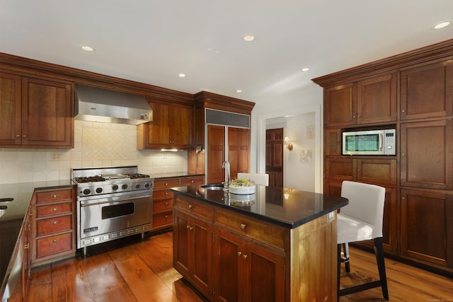 kitchen featuring premium appliances, wall chimney exhaust hood, dark wood-style flooring, a sink, and recessed lighting
