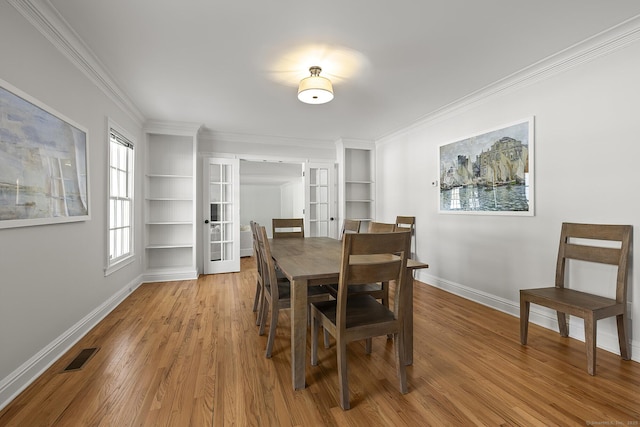 dining space featuring french doors, crown molding, built in features, and light wood-type flooring