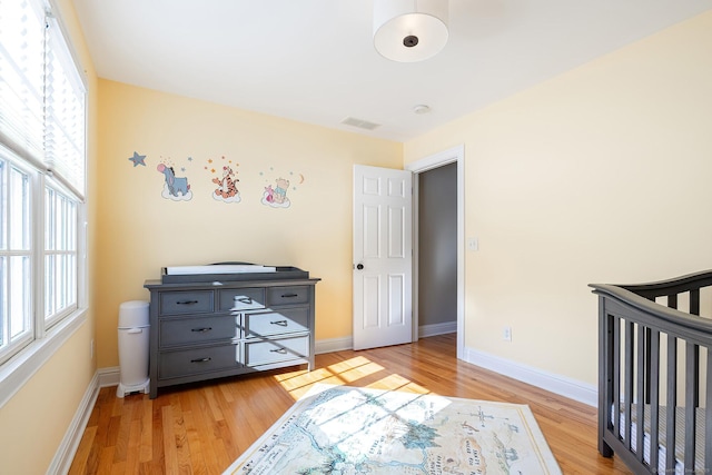 bedroom with light hardwood / wood-style flooring, multiple windows, and a crib