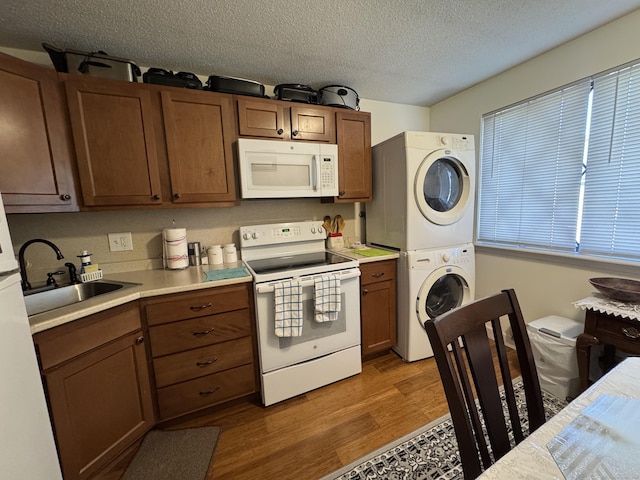 kitchen with stacked washing maching and dryer, wood-type flooring, sink, white appliances, and a textured ceiling