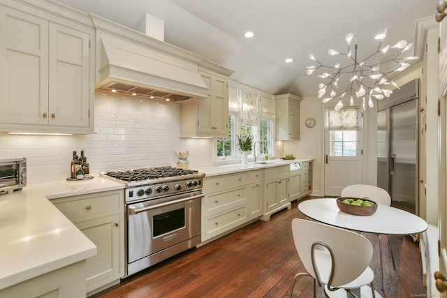 kitchen featuring sink, premium appliances, cream cabinets, custom range hood, and decorative light fixtures