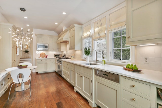 kitchen with lofted ceiling, sink, custom exhaust hood, decorative light fixtures, and stainless steel appliances