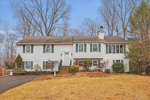 bi-level home with a chimney, a front yard, and fence