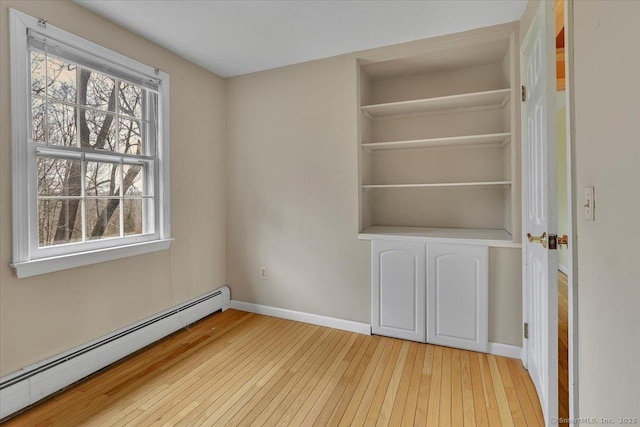 unfurnished bedroom with a baseboard heating unit, light wood-style flooring, and baseboards