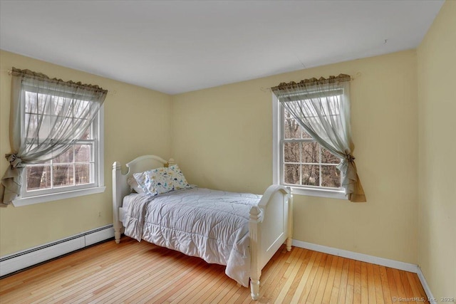 bedroom featuring a baseboard heating unit, wood-type flooring, and baseboards