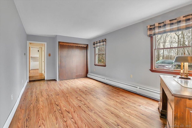 unfurnished bedroom featuring light wood-style flooring, baseboards, baseboard heating, and a closet