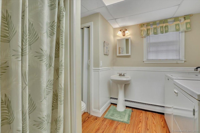 bathroom with a drop ceiling, toilet, a sink, wood finished floors, and independent washer and dryer